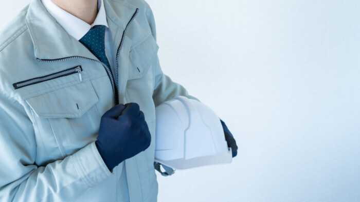 作業服にネクタイの男性。ヘルメットを抱える。建設業イメージ